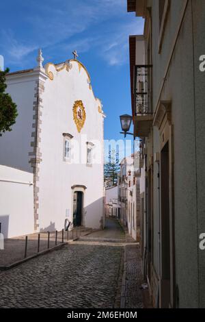 Una vista dell'esterno, imbiancata, semplice, entrata dalla facciata semplice. Nella chiesa cattolica di Igreja de Santiago a Tavira, Algarve, Portogallo, Europa. Foto Stock