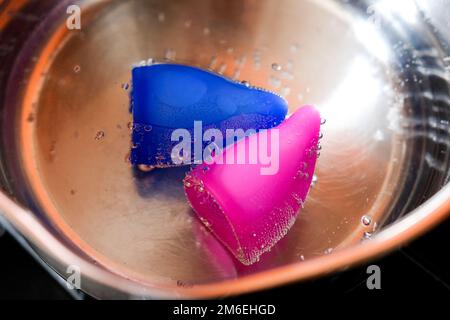 Cura della tazza mestruale. I prodotti siliconici per le donne bollono Foto Stock