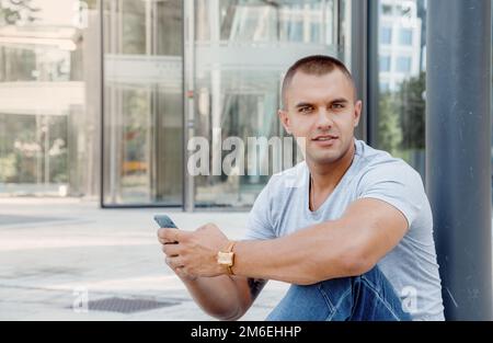 Giovane uomo che parla su un telefono cellulare. Un ragazzo con un tatuaggio sul braccio. Bel ragazzo in città. Foto Stock