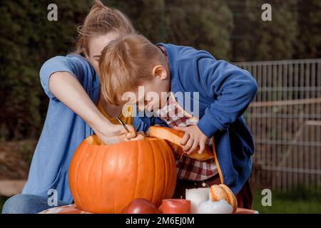 Un ragazzo e sua madre tagliarono una zucca. Una giovane madre e un figlio stanno preparando una zucca per Halloween. Preparandosi per Halloween. Pelare Foto Stock