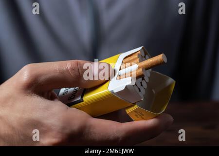 Una mano di mans che tiene fuori un pacco aperto di sigarette. Foto Stock