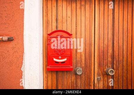 Cassetta postale rossa vintage appesa su una porta di legno in una casa sulla strada in attesa di consegna della posta Foto Stock