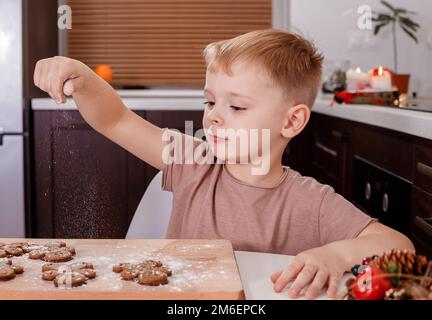 Bambino dipingendo l'uomo di pan di zenzero. Idee regalo di Natale fatte a mano. Cucina decorata per Natale. Scatto orizzontale. Foto Stock