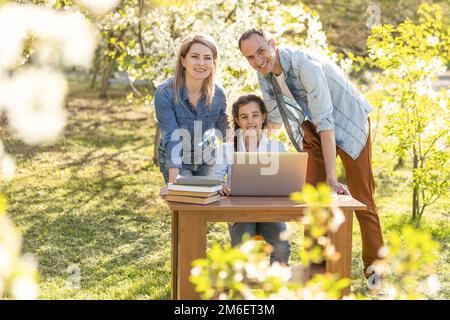 bambina con mamma e papà che studiano su un computer portatile all'aperto Foto Stock