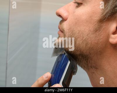 Un uomo taglia una barba ricostruita sul mento usando un regolacapelli Foto Stock