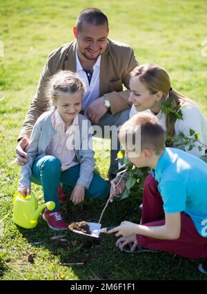 Famiglia genitori e bambini piantare alberi in siping nel parco estivo Foto Stock