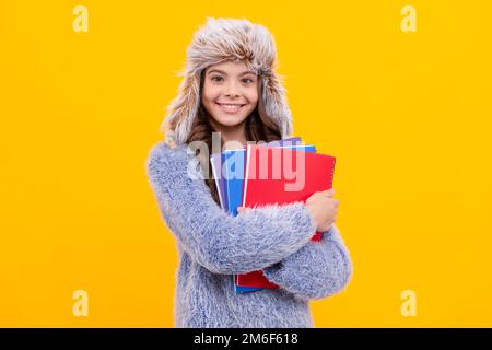 bambino felice in maglione e cappello con libro da lavoro su sfondo giallo, di nuovo a scuola Foto Stock