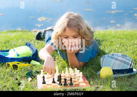 Bambino piccolo giocare a scacchi nel parco. Bambino ragazzo gioco da tavolo all'aperto. Pensare bambino brainstorming e l'idea nel gioco di scacchi. Foto Stock