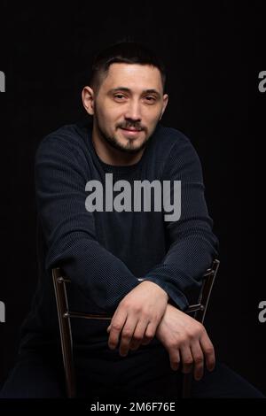 Ritratto di un uomo sorridente di trent'anni di caucasico aspetto in un maglione normale su sfondo nero Foto Stock