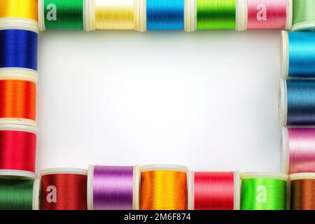 Telaio in rocchetti con fili da cucire colorati su sfondo bianco, vista dall'alto. Spazio libero per il testo. Foto Stock