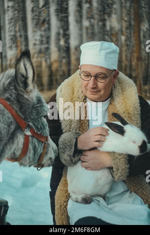 Veterinario medico premuroso tiene un coniglio in braccio e un asino accanto a lui. Il veterinario esamina gli animali Foto Stock