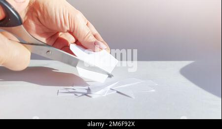 La mano di una donna taglia un foglio di carta bianca con forbici e taglia gli angoli. Primo piano, concetto fai da te Foto Stock