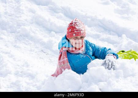 La ragazza che ha rotolato giù la collina ha tutta la sua faccia nella neve, la ragazza sembra divertente nel telaio Foto Stock