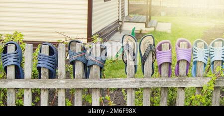Scarpe estive infradito infradito per una famiglia felice e amichevole appendere su una recinzione di legno all'aperto in una giornata di sole estate Foto Stock