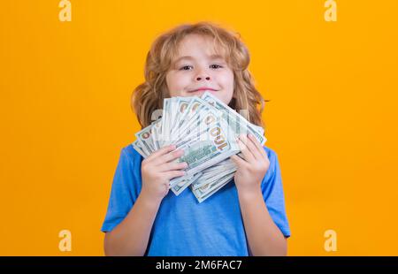 Capretto che mostra le fatture del dollaro dei soldi, sognando levante in piedi dei ricchi contro lo sfondo giallo isolato dello studio. Foto Stock