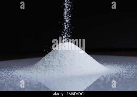primo piano di sabbia che cade in un mucchio su sfondo nero. Foto Stock