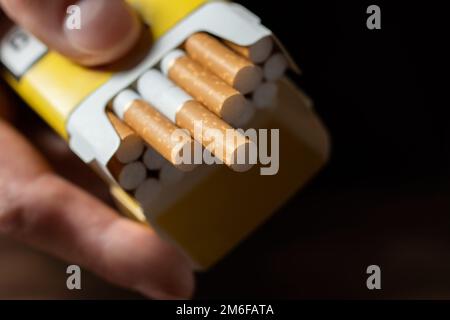 Una mano di mans che tiene fuori un pacco aperto di sigarette. Foto Stock