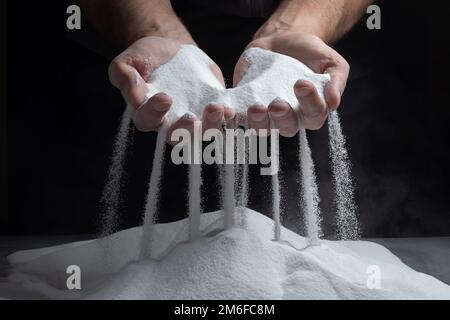 Le mani degli uomini tengono la sabbia nelle loro palme e versando grani di sabbia attraverso le loro dita. Concetto del flusso di vita Foto Stock