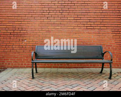 Una panca di parco vuota davanti ad una parete di mattoni vuota Foto Stock