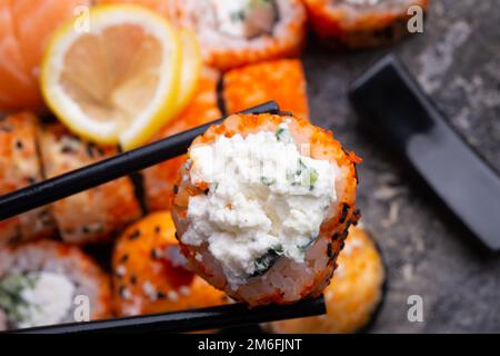 Sushi roll con formaggio morbido che tiene in bastoncini. panini sushi serviti al vassoio grigio piatto. primo piano Foto Stock