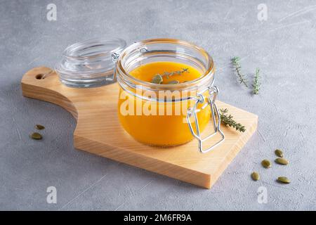 Zuppa di purea di zucca con semi di zucca e timo in un vaso di vetro su un tavolo da cucina di legno. Il concetto di nutrizione sana da verdure di stagione. S Foto Stock