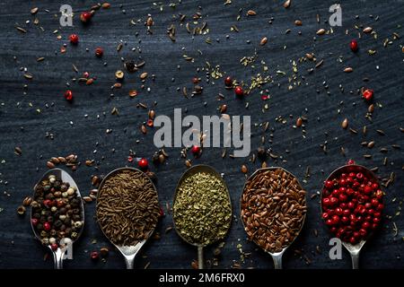 Vecchi cucchiai di metallo con diversi tipi di semi e spezie su sfondo nero. Giacitura piatta. Vista dall'alto. Concetto di cibo. Fotografia di cibo di umore scuro. Foto Stock