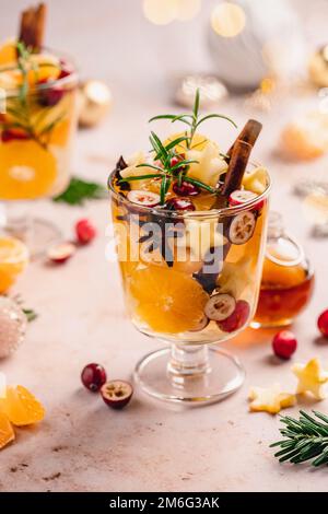 Bicchiere di vino bianco caldo tritato con arance, mele, cannella, mirtilli rossi e spezie su fondo bianco. Bevande calde invernali. Vista laterale ravvicinata. Foto Stock