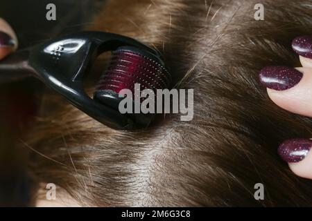 Donna che usa il rullo derma microneedle sulla testa per stimolare la crescita di nuovi capelli. Trattamento semplice ed economico per il cuoio capelluto sano. Foto Stock