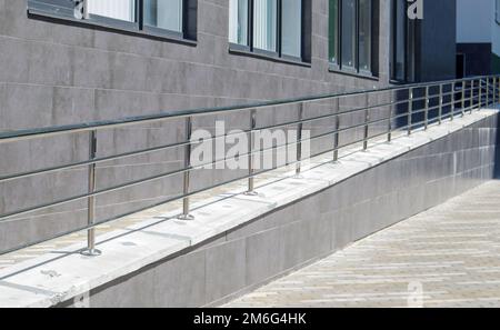 Una rampa con corrimano in acciaio inox per sedie a rotelle, biciclette e passeggini con bambini davanti all'edificio. Corrimano f Foto Stock