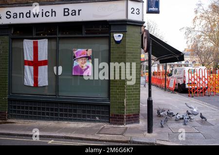 Faccia della Regina Elisabetta II accanto ad una bandiera di Saint Georges Cross nella vedova di un bar sandwich a Smithfields il 5th dicembre 2022 a Londra, Regno Unito. Foto Stock