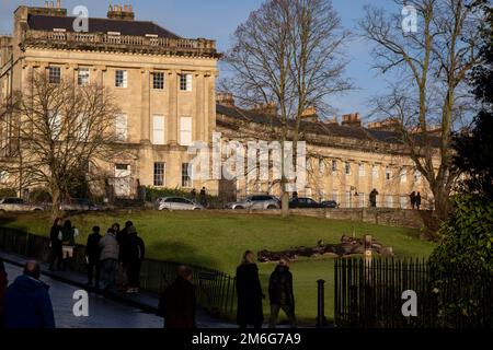 Le persone si riuniscono per scattare foto e vedere la Royal Crescent il 29th dicembre 2022 a Bath, Regno Unito. Il Royal Crescent a Grade i edificio storico costituito da una fila di 30 case a schiera costruito in una mezzaluna che è stato progettato dall'architetto John Wood, il più giovane e costruito tra il 1767 e il 1774. E' uno dei più grandi esempi di architettura georgiana che si possa trovare nel Regno Unito. Bath è una città nella contea del Somerset, conosciuta e chiamata per i suoi bagni di costruzione romana, e l'architettura georgiana fatta dalla pietra locale di Bath color miele. La città divenne un sito patrimonio dell'umanità nel 1987, un Foto Stock