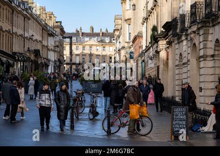 Persone, tra cui acquirenti e visitatori fuori e fuori su Milsom Street, nel centro della città, il 29th dicembre 2022 a Bath, Regno Unito. Bath è una città nella contea del Somerset, conosciuta e chiamata per i suoi bagni di costruzione romana, e l'architettura georgiana fatta dalla pietra locale di Bath color miele. La città è diventata patrimonio mondiale nel 1987 e nel 2021 è stata aggiunta al patrimonio mondiale transnazionale noto come le “grandi città termali d’Europa”. Foto Stock