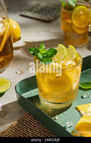 Tradizionale tè freddo fatto in casa con limone, menta e ghiaccio in bicchieri. Bevanda fredda estiva su sfondo verde. Concetto di sano cibo estivo. Messa a fuoco selettiva Foto Stock