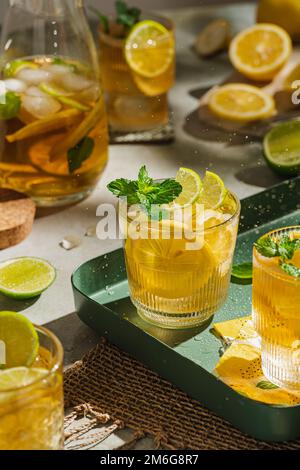 Tradizionale tè freddo fatto in casa con limone, menta e ghiaccio in bicchieri. Bevanda fredda estiva su sfondo verde. Concetto di sano cibo estivo. Messa a fuoco selettiva Foto Stock