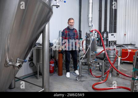 Uomo in camicia a quadri che lavora al birrificio e che guarda soddisfatto Foto Stock