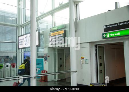 Persona che cammina attraverso il corridoio dell'aeroporto con le indicazioni per il trasferimento del volo, il controllo del passaporto, gli arrivi, il ritiro bagagli e i passeggeri che ritornano. Londra Foto Stock