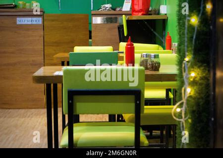 Tavoli e sedie sono disposti in un buon negozio di cibo interno fresco e luminoso con un tema di colore scuro. Foto Stock