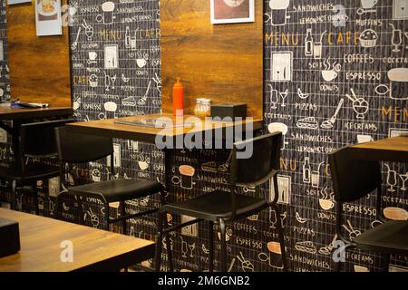 Tavoli e sedie sono disposti in un buon negozio di cibo interno fresco e luminoso con un tema di colore scuro. Foto Stock