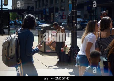 Un uomo nero chiede cambiamenti e donazioni al pubblico sotto il sole in un angolo di strada nella zona del Millennium Park di Chicago in estate Foto Stock