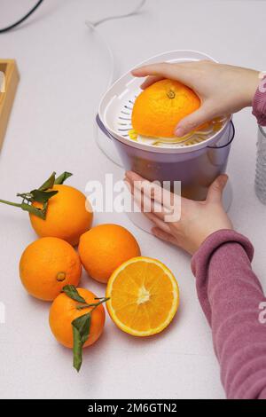 le mani della donna schiacciano le arance in una centrifuga Foto Stock