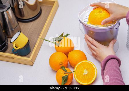 le mani della donna schiacciano le arance in una centrifuga Foto Stock