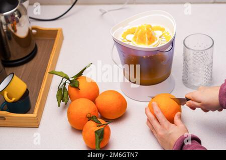 le mani della donna tagliano un arancio con un coltello per spremiarlo Foto Stock