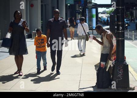 Un uomo nero chiede cambiamenti e donazioni al pubblico sotto il sole in un angolo di strada nella zona del Millennium Park di Chicago in estate Foto Stock