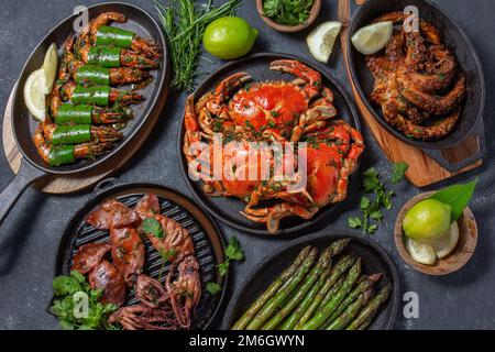 Set di piatti di pesce. Granchi, polpi, calamari e gamberetti sulle teglie e piatti di ghisa su fondo nero. Vista dall'alto Foto Stock