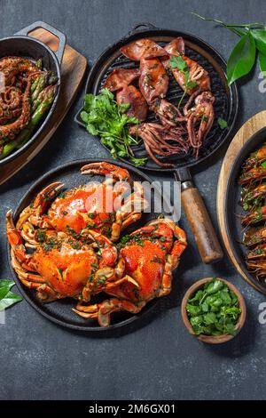 Set di piatti di pesce. Granchi, polpi, calamari e gamberetti sulle teglie e piatti di ghisa su fondo nero. Vista dall'alto Foto Stock