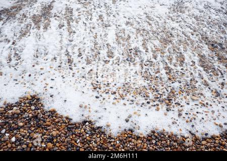 Un primo piano come il surf di mare schiumoso si bagna su una spiaggia di gente sulla costa meridionale inglese Foto Stock