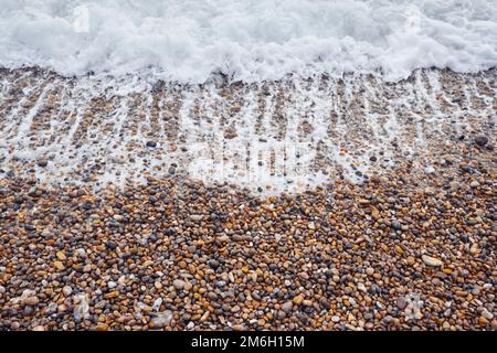 Un primo piano come il surf di mare schiumoso si bagna su una spiaggia di gente sulla costa meridionale inglese Foto Stock