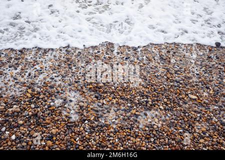 Un primo piano come il surf di mare schiumoso si bagna su una spiaggia di gente sulla costa meridionale inglese Foto Stock