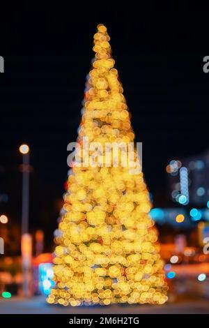 Grande albero di Natale nella città di notte. Immagine sfocata con effetto bokeh. Immagine sfocata sullo sfondo Foto Stock