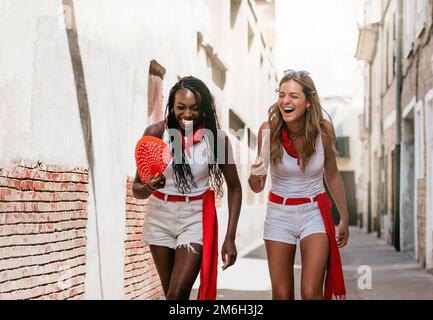due giovani donne caucasiche e afro-americane si godono le feste tradizionali in una città spagnola. concetto di diversità, tolleranza e divertimento. Foto Stock